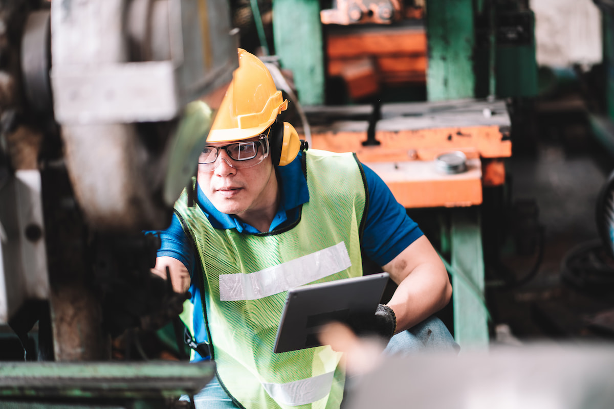 Person in hardhat and high visibility vest inspecting machinery in a manufacturing plant