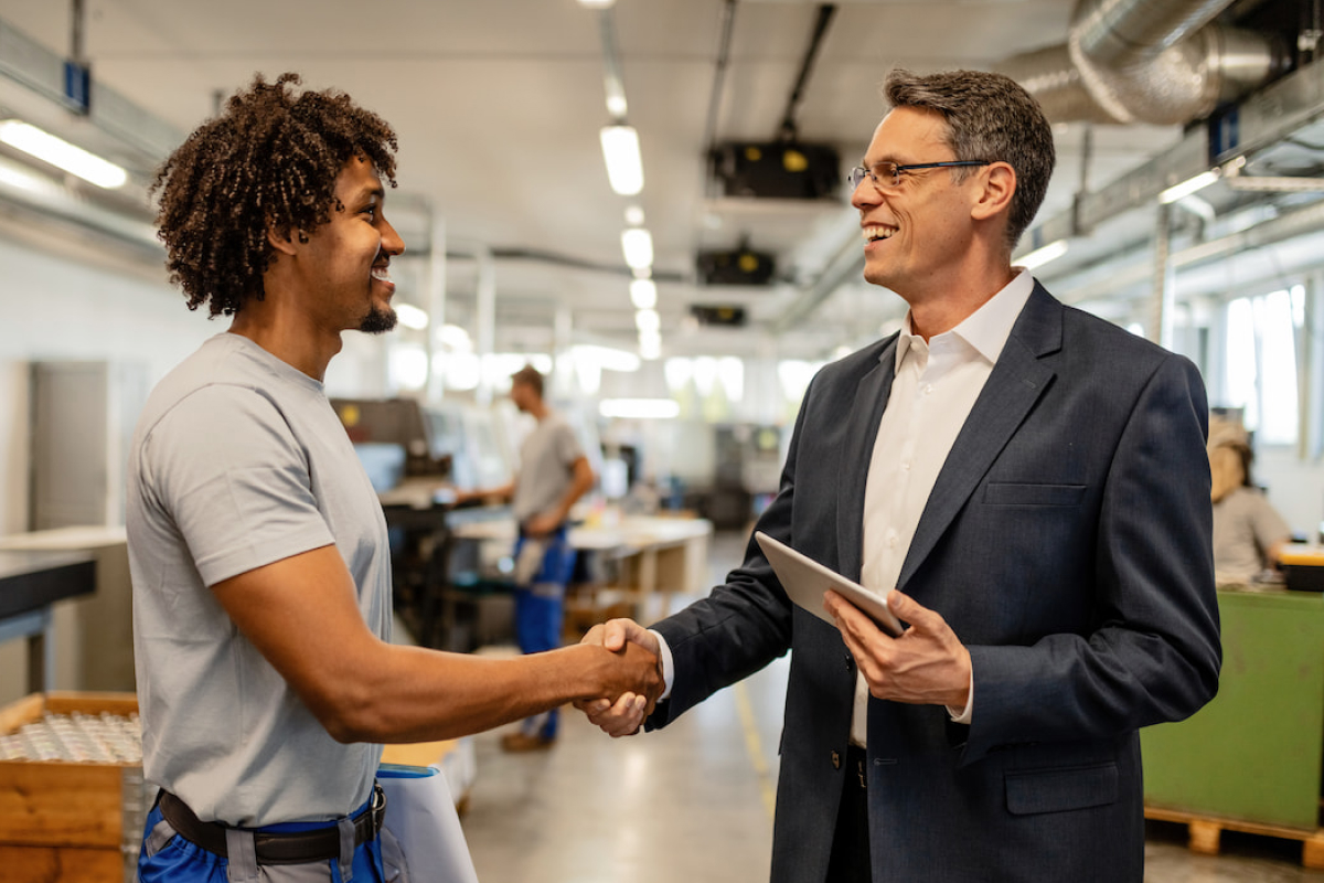 A leadership member in suit shaking hands and smiling at employee in manufacturing plant