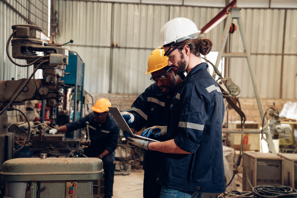 Two employees in hardhats working together on a laptop